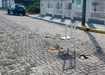 Moradores usam cadeira para sinalizar buraco em rua, em Tijucas