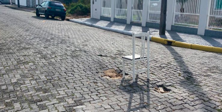 Moradores usam cadeira para sinalizar buraco em rua, em Tijucas